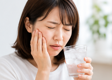 冷たいものがしみて頬に手を当てる女性、知覚過敏のイメージ